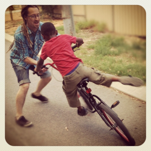 Jarrod McKenna helping one of his First Home Project roommates learn to ride a bike.