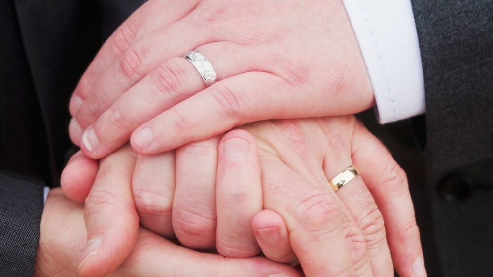 Two men holding hands with wedding rings