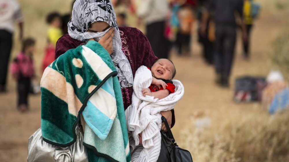 A young mother crosses the border from Syria and becomes a refugee. She carries her one-month-old son, Hamid. “Since he was born there has been non-stop bombing every day.”