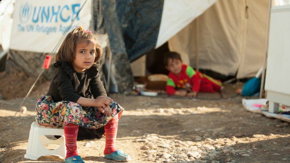 A young girl sits outside a UNHCR tent in war-ravaged Syria