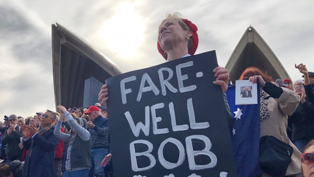 Woman holds farewell sign for Bob Hawke on Opera House foreshore