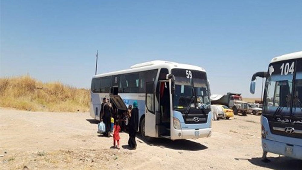 Displaced people board a bus to return to their home areas across Nineveh province in July 2019