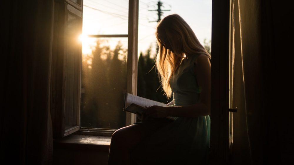 Girls sits in bedroom window with book. Image: Yuri Efremov/ Unsplash