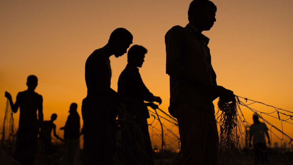 Men carry baskets of coal from the docked ships and carry by hand (and head) to trucks being loaded nearby. The trek is about a hundred meters over planks of wood that link boats in line waiting to be unloaded. Chittagong Bangladesh. Image by Simon Lister, used with permission.