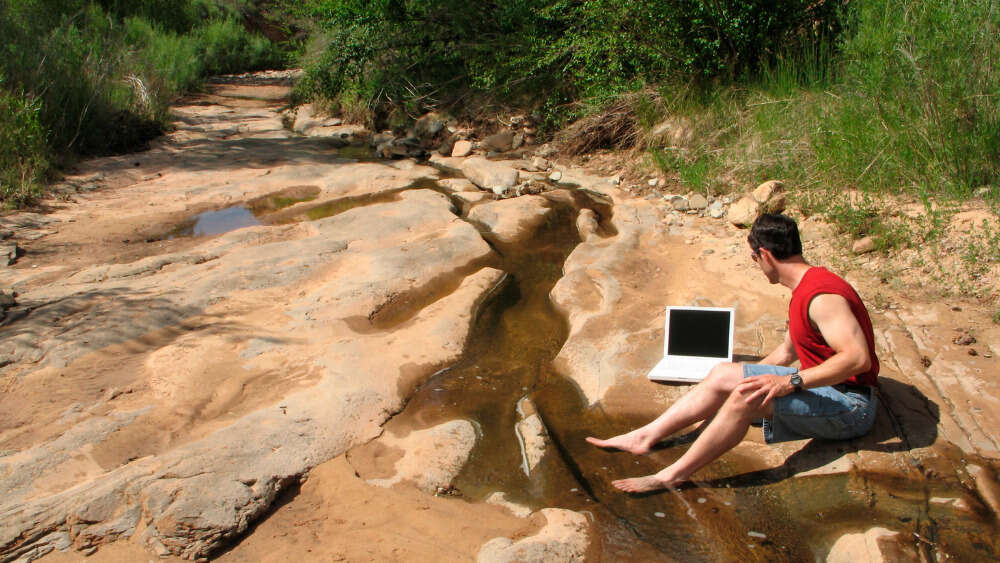 Man on laptop by desert stream