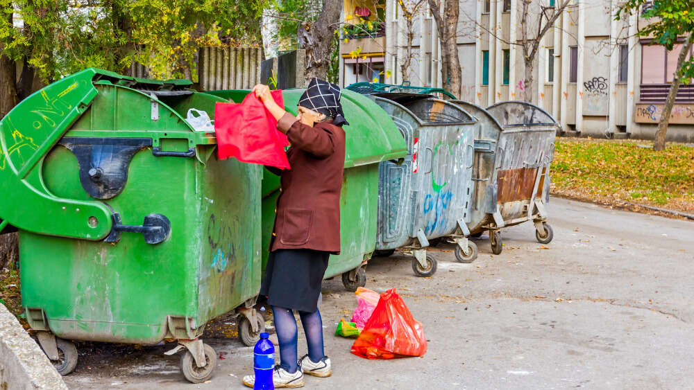 Woman looks through garbage bin