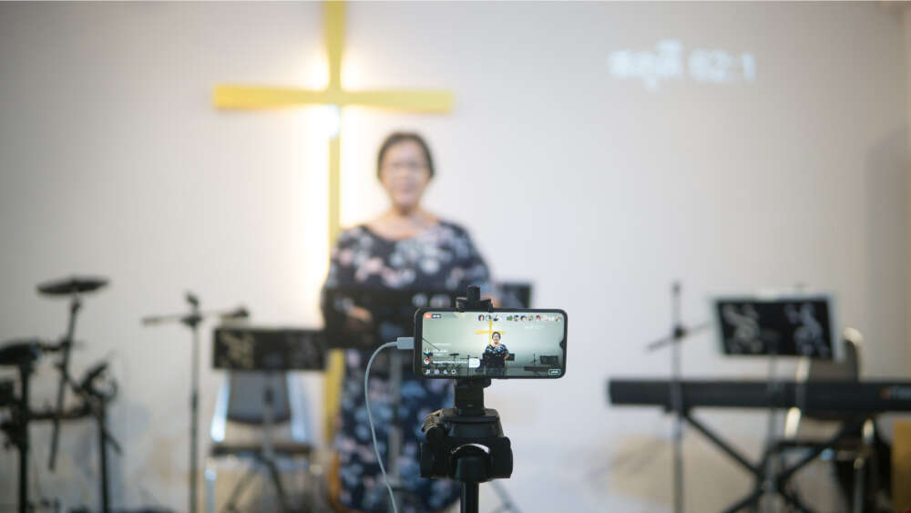 Woman preaches in front of a church and camera